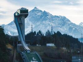 The Bergisel Ski Jump in Innsbruck, Austria, features modern architecture with an observation deck, surrounded by forests and alpine mountains. photo