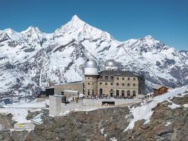 The Gornergrat Observatory with silver domes on a rocky ridge, surrounded by snowy peaks, with the Matterhorn visible in clear daylight. photo