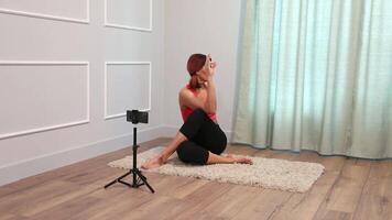 middle aged woman doing yoga standing on the floor at home and also broadcasting to her followers using a smartphone mounted on a tripod video