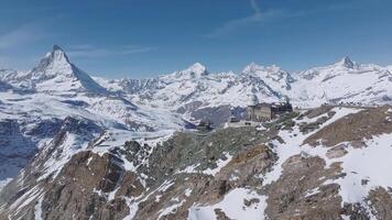 Aerial view of Zermatt ski resort with Matterhorn peak, Gornergrat observatory, snowy alpine terrain, and a clear blue sky in smooth motion. video