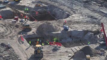 Workers operate machinery and work on reinforced concrete structures at an active construction site with cranes, excavators, and sandy terrain. video