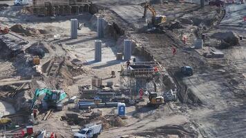 Active construction site in Riga showing excavators, cranes, workers, concrete pillars, scaffolding, and vehicles in motion with marked safety zones. video