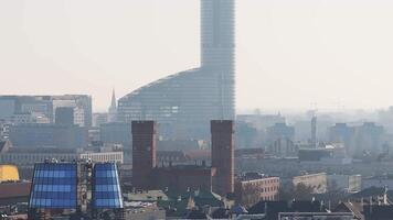 Aerial view of Wroclaw, Poland, showing a red brick tower, a glass building with blue panels, a curved glass dome, and a crane under a clear sky. video