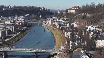 Antenne Aussicht von salzburg, Österreich, mit das salzburg Dom, ein fließend Fluss mit ein Brücke, und ein Hintergrund von Hügel und Schnee gekappt Berge. video
