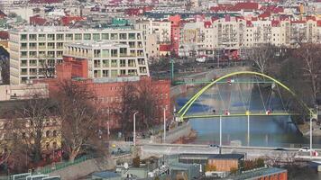 Aerial view of Wroclaw, Poland, showing a yellow arched pedestrian bridge over a calm river, surrounded by modern and historic architecture in a colder season. video