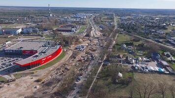 Aerial view of active construction in Riga, Latvia, showing earthworks, machinery, a smokestack, and a partially built roadway under clear skies. video