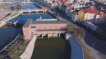Aerial pan over Wroclaw, Poland, showing a canal with a lock system, a red brick building, an arched bridge, and urban architecture. video