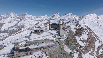 Aerial view of Gornergrat observatory on a rocky ridge with snow covered peaks, including the Matterhorn. Camera moves smoothly, showing alpine terrain. video