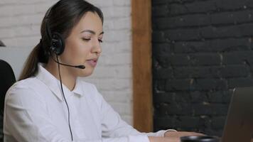 Customer service representative in headset communicating via laptop, engaged in support or virtual assistance in modern office setting. 9 video