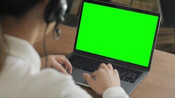 Female support agent in headset working remotely on a laptop with green screen, ideal for mockup or design replacement in customer service context. video