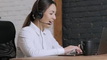 Customer service representative in headset communicating via laptop, engaged in support or virtual assistance in modern office setting. 14 video