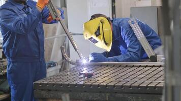 Man with assistant wearing mask welding in a workshop. Metal workers use manual labor. Skilled welder. Welder is welding the stainless steel pipes in the factory. welder Industrial part in factory. video