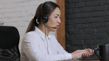 Customer service representative in headset communicating via laptop, engaged in support or virtual assistance in modern office setting. 10 video