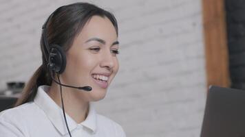 Customer service representative in headset communicating via laptop, engaged in support or virtual assistance in modern office setting. 2 video