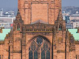 Liverpool Cathedral's Gothic architecture with red sandstone, copper roof, and stained glass window, set against modern urban buildings in Liverpool, England. photo