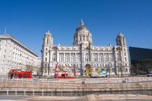 The Port of Liverpool Building in England features Edwardian Baroque architecture, colorful art installations, red double decker buses, and a clear blue sky. photo