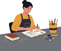 Woman sketching in notebook while seated at a table with art supplies nearby vector