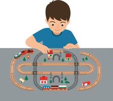 Young boy arranging colorful toy train tracks on a table with buildings and trees vector
