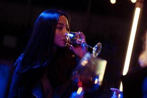Woman enjoying a drink in a trendy venue during a nighttime social gathering with vibrant lighting photo