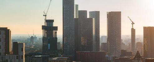 Aerial view of Manchester, UK, featuring modern skyscrapers, glass clad buildings, and a crane atop an unfinished high rise on a sunny day. photo