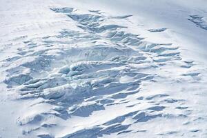 A glacier near Zermatt, Switzerland, featuring deep crevasses, compacted ice layers, and bluish hues contrasting with surrounding snow covered terrain. photo