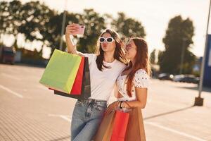 Two beautiful, women in casual clothes, are holding shopping bags, outdoors photo