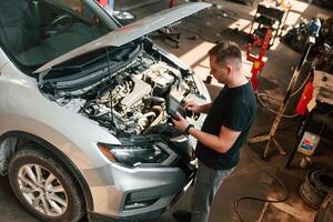Holding the, tablet. Man is works in the, automobile repairing salon photo