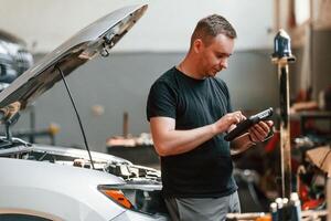 Using the tablet. Man is works in the automobile repairing salon photo
