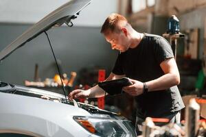 Using the ,tablet. Man is, works in the automobile repairing salon photo