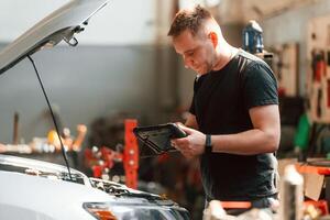 Using ,the tablet.. Man is works in the automobile repairing salon photo