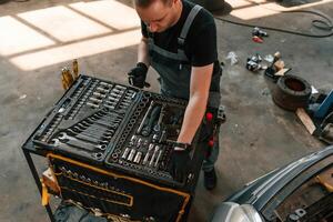 Top view of employee that standing, by the toolbox. Man is works in the automobile repairing salon photo