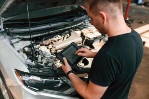 Holding, the tablet. Man is works in the automobile repairing salon photo