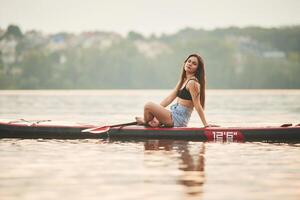 Forest ,and, houses on background. Young woman is on sup boards in the lake photo