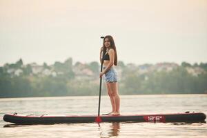 Forest ,and houses on background. Young woman is on sup boards in the lake photo
