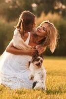 Conception, of ,love and care. Mother with her daughter and cute dog are on the field outdoors photo
