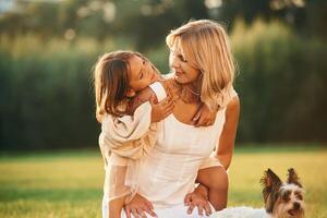 Conception, of ,love, and care. Mother with her daughter and cute dog are on the field outdoors photo