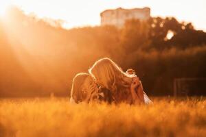 Illuminated by, sunlight, lying down. Mother with her daughter and cute dog are on the field outdoors photo