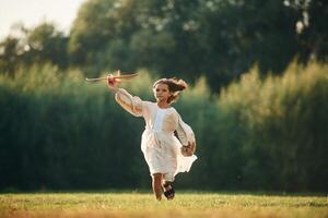 Running, with, toy plane. Little girl is on the summer field outdoors photo