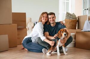Sitting and smiling. Young,couple, with dog are moving to new home photo