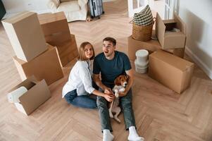 Sitting and smiling,. Young couple with dog are moving to new home photo