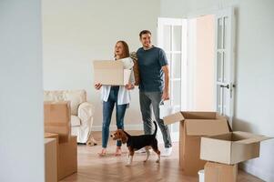 In the big, room, with boxes in hands. Young couple with dog are moving to new home photo