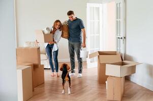 In, the big room, with boxes in hands. Young couple with dog are moving to new home photo