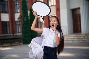 Sticker with thoughts, copy space for, text. School girl in uniform is outdoors near the building photo