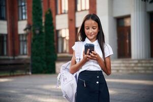 Phone in hands. School girl in uniform ,is outdoors near the building photo