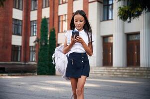 Phone ,in, hands. School girl in uniform is outdoors near the building photo