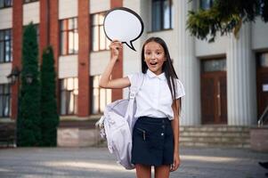 Holding sign with copy, space, for text. School girl in uniform is outdoors near the building photo
