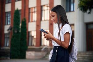 Holding smartphone. School ,girl in ,uniform is outdoors near the building photo
