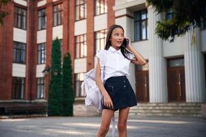 Phone in hands. School, girl in ,uniform is outdoors near the building photo