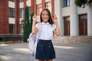 Fingers crossed. School girl, in uniform is outdoors near the building photo