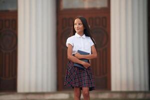 Conception of knowledge.,. School girl in uniform is outdoors near the building photo